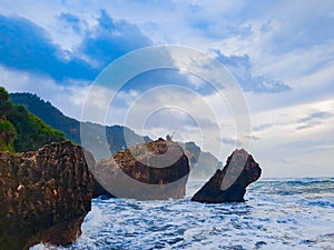 A fisherman sitting on a rock formation while big long waves flo