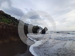 A fisherman sitting on a rock formation while big long waves flowing.