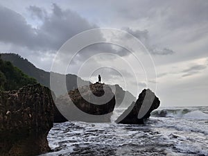 A fisherman sitting on a rock formation while big long waves flowing.