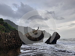 A fisherman sitting on a rock formation while big long waves flowing.