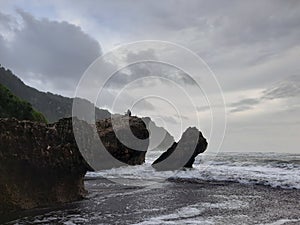 A fisherman sitting on a rock formation while big long waves flowing.