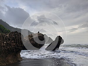 A fisherman sitting on a rock formation while big long waves flowing.