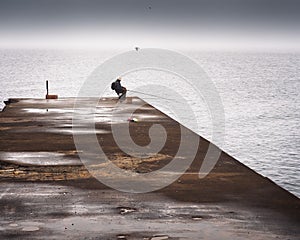 Fisherman sleeping on a pier on a foggy day at sea