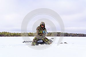 A fisherman in special clothes catches fish in winter on the lake. The concept of survival in the wild in winter