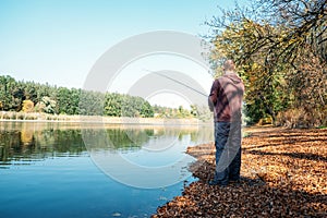 Fisherman with spinning rod on the autumn lake. fisherman with spinning in his hands catching fish at sun day. Fisherman