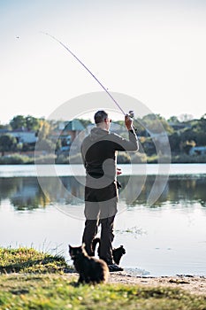 Fisherman with spinning rod and cat near him on nature background. Angler man with fishing spinning or casting rod by