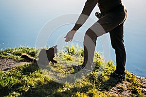 Fisherman with spinning rod gives the cat a fish perch on nature background. Angler man with fishing spinning or casting