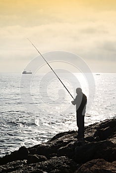 A fisherman standing with the fishing rod in his hand, he is on