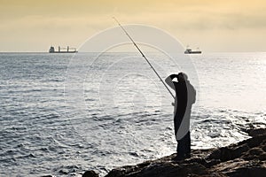 A fisherman standing with the fishing rod in his hand, he is on