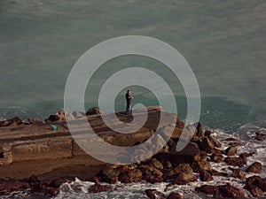 Fisherman standing on a rock in front of the sea