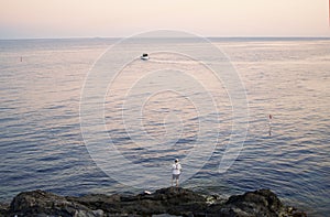 Fisherman standing at the seashore hooks a fish against sunset. Sportsman holds a fishing rod and reel in a hooked fish. Spin