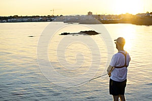 Fisherman standing at the seashore hooks a fish against sunset. Sportsman holds a fishing rod and reel in a hooked fish. Spin