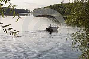 Fisherman are swiming on the boat. Wide river flowing across green forest. Fall. Evening. Reflections of trees in the calm water.