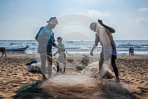 Fisherman taking the fish from Nylon Fishing net. Indian fisherman working on their net on beach sand