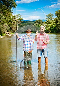 Fisherman and trophy trout. Young man and old mature man fly fishing. Difference between fly fishing and regular fishing
