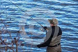 Fisherman in waders catches pike in the lake photo
