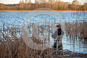 Fisherman in waders catches pike in the lake