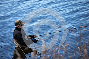 Fisherman in waders catches pike in the lake photo