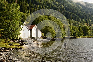 Fisherman in water Norwegian Fjord with boatshed and forest in background