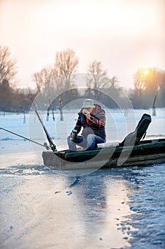 Fisherman in winter fishing drink tea on frozen lake
