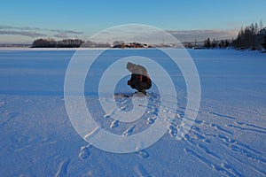 Fisherman on winter fishing. A man sits near a hole in a frozen lake waiting for a bite. Snow on ice. Bottom fishing for