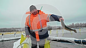 A fisherman in winter garb beams with success, holding a speckled trout before the dormant landscape of a fish breeding