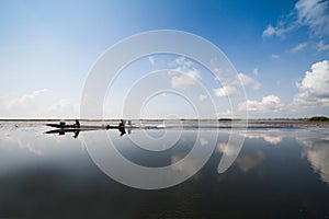 Fisherman in wooden boat crusing in the lake with reflection with cloudy blue sky background