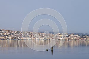 A fisherman at work bending in the flat sea water that reflects the houses of Sant `Antioco in Sardinia