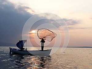 Fishermans throwing net to sea on sunset