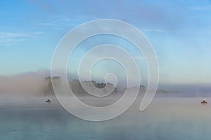 Fishermen on boats early in the morning at dawn in the fog