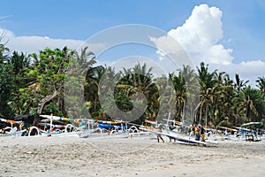 Fishermen carry a boat on a virgin beach in Bali. Fishing boats on white sand. Coconut trees and blue sky with clouds on