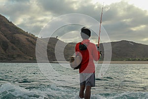 Fishermen catch fish at low tide. View from the back of guy with fishing rods in the water. Close up of Indonesian man