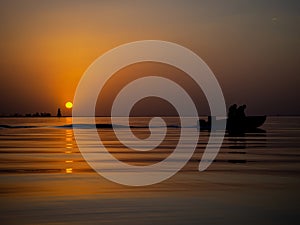 Fishermen in a fishing boat on background of a Golden sunset on sea. Full calm, calm surface of water in ocean with a