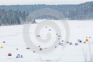 Fishermen fishing on a frozen lake in winter with fishing pole or rod, ice auger, various equipment