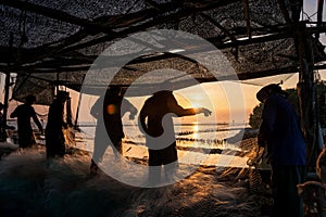Fishermen pull fishing net by the sea at sunset