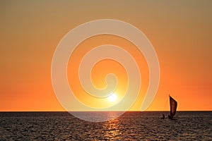 Fishermen in a sailboat at a beautiful warm orange glow sunset