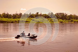 Fishermen sailing fast at rubber powerboat by river making trace at tranquil water surface . Fishing background. Retro  noise
