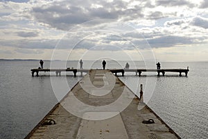 Fishermen waiting on a pier on a winter day. Cloudy sky and calm sea.