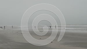 fishermen walking over a wide sand beach in thick fog