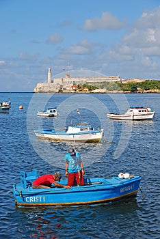 Fishermen working on a small blue boat with Morro Castle in the background