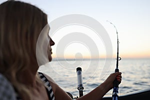 Fisherwoman holds spinning rod in her hands and looking at sea while fishing from boat.