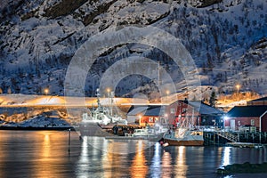 Fishing boat anchored at dock in illuminated fishing village on coastline at Lofoten Islands