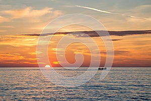 Fishing boat on the background of incredible golden sunrise, clouds and rising sun.