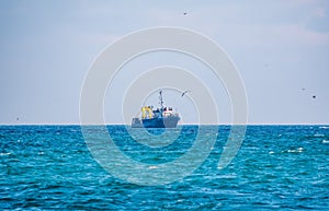 Fishing boat in blue sea and clear sky with birds flying overhead