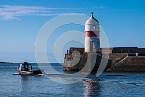 Fishing boat heading out to sea past harbor and lighthouse