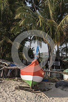 Fishing boat painted in the colors of the Indian flag under the palm trees on the beach in Goa in India