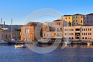 Fishing boat pass by Grand Arsenal in Old Venetian harbour, Chania, Crete, Greece. Sunrise view of quay and sailing