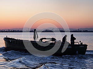 fishing boat retuning home at sunset with evening sky with waves