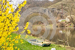 A fishing boat on the river shore surrounded by trees whiteout leaves spring day