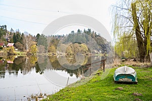 A fishing boat on the river shore surrounded by trees whiteout leaves spring day